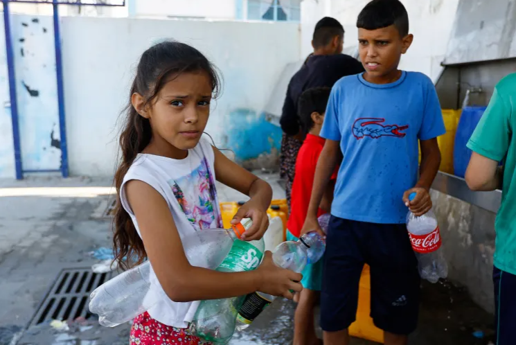 Trẻ em Palestine tụ tập lấy nước từ vòi công cộng vào chai trong bối cảnh xung đột với Israel ở Khan Younis, phía nam Dải Gaza [Ibraheem Abu Mustafa/Reuters]