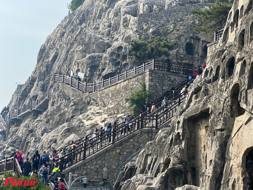 Hang động Long Môn Sơn, được xây dựng từ năm 493 dưới thời Bắc Ngụy và tiếp tục mở rộng vào thời nhà Đường. Đây là hai triều đại này nổi tiếng tôn sùng đạo Phật và tích cực xây dựng nhiều công trình Phật giáo, vì vậy hang động Long Môn là kiệt tác chạm khắc tiêu biểu cho thời kỳ phát triển rực rỡ của Phật giáo ở Trung Quốc thời kì này. Trong ảnh: Du khách đang leo bậc thang lên địa điểm nổi tiếng nhất của quần thể Long Môn Sơn là khu vực tượng Phật Lư Xá Na. 
