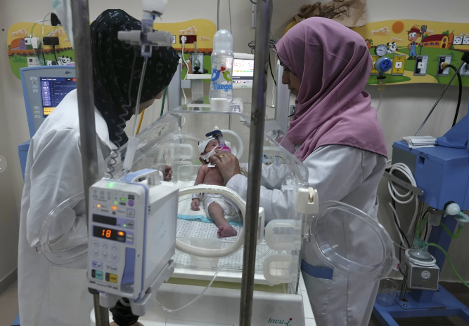 Một em bé sinh non vặn vẹo trong lồng ấp thủy tinh ở khu sơ sinh của Bệnh viện al-Aqsa ở trung tâm Dải Gaza. Cậu bé kêu lên khi đường truyền tĩnh mạch được nối vào cơ thể nhỏ bé của mình. Máy thở giúp anh thở trong khi ống thông truyền thuốc và màn hình hiển thị các dấu hiệu sinh tồn mong manh của anh.  Cuộc sống của anh phụ thuộc vào dòng điện liên tục, có nguy cơ cạn kiệt trừ khi bệnh viện có thể bổ sung thêm nhiên liệu cho máy phát điện. Khi máy phát điện ngừng hoạt động, giám đốc bệnh viện Iyad Abu Zahar lo ngại rằng những đứa trẻ trong phòng bệnh không thể tự thở sẽ tử vong.  Ông nói: “Trách nhiệm đối với chúng tôi là rất lớn.