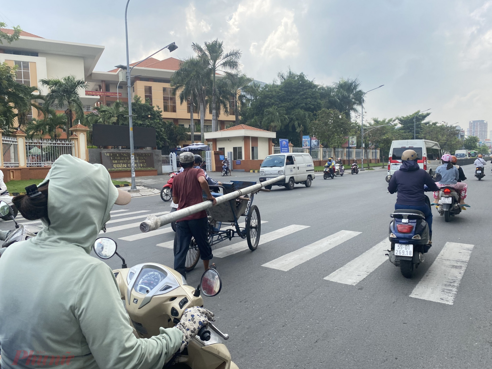 Người lái xích lô một tay giữ thanh sắt dài một tay điều khiển phương tiện giữa dòng xe cộ đông đúc trên đường Lũy Bán Bích, quận Tân Phú.