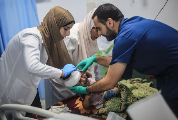 Một thành viên của Hội Chữ thập đỏ giúp các bác sĩ Palestine ở Khan Younis kiểm tra một đứa trẻ bị thương hôm thứ Ba. Ảnh: Mohammed Talatene/Avalon