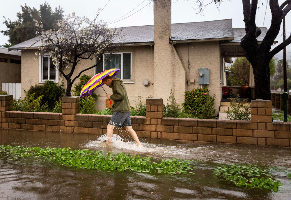 Một người đi bộ băng qua nước lũ trong cơn mưa bão ở Santa Barbara, California vào ngày 4/2 - Ảnh: Ethan Swope/AP