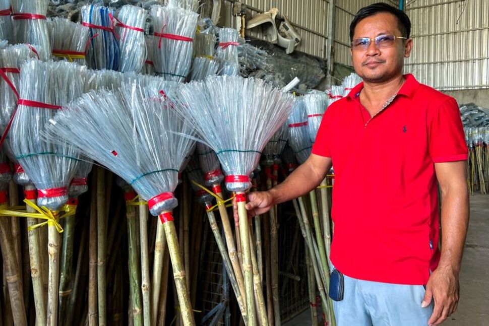 Ông Has Kea giới thiệu những chiếc chổi thành phẩm được tái sinh từ rác thải nhựa - Ảnh: Reuters