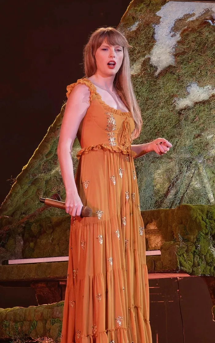 Điệu đà và cổ điển như một cô gái thôn quê, Taylor khoác lên mình chiếc váy diềm bèo màu cam đất khi thể hiện các ca khúc trong album Evermore.
