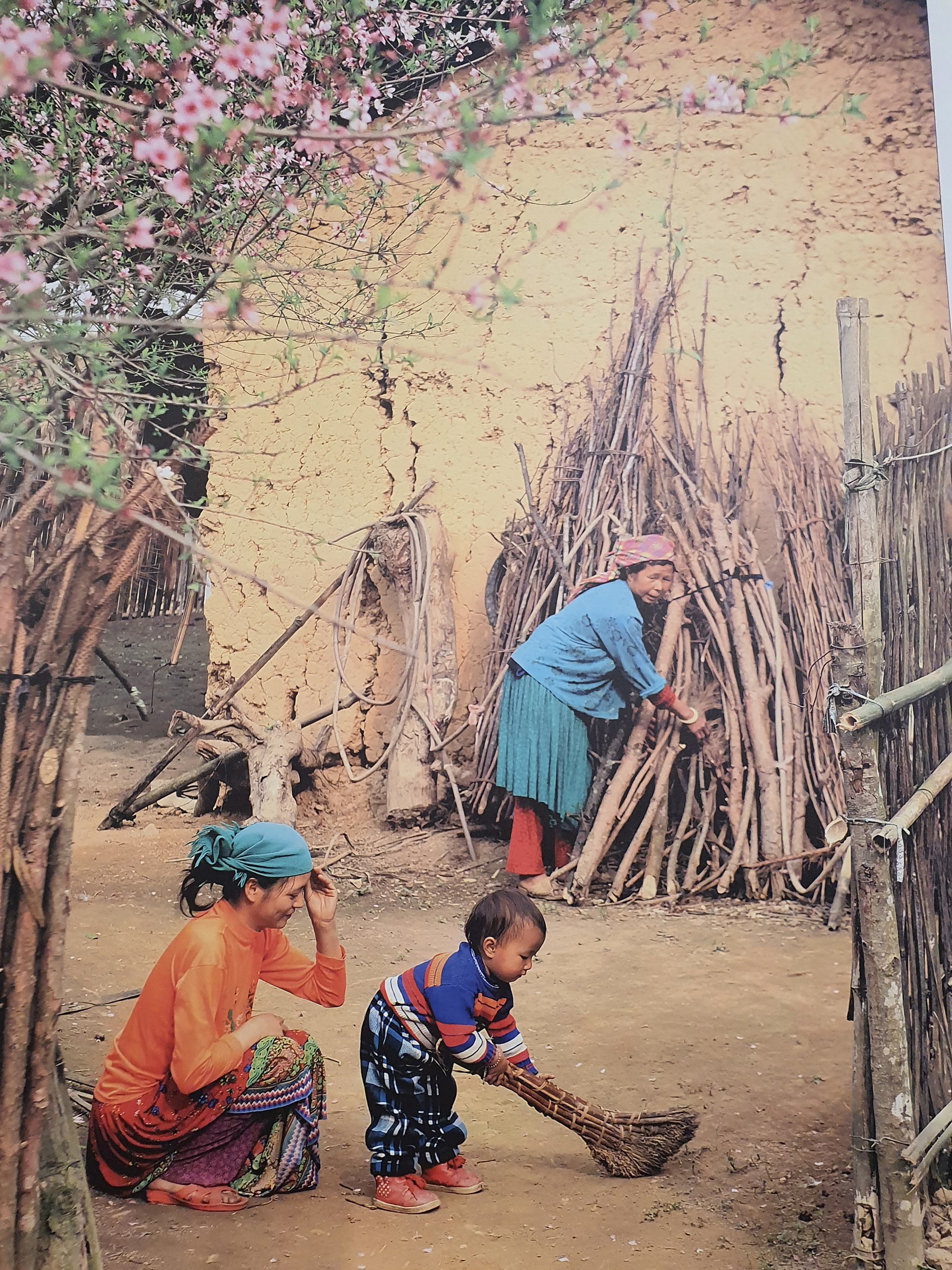 Bé được mẹ dạy quét sân. Ảnh chụp tại sân nhà một gia đình dân tộc ở Yên Minh, Hà Giang