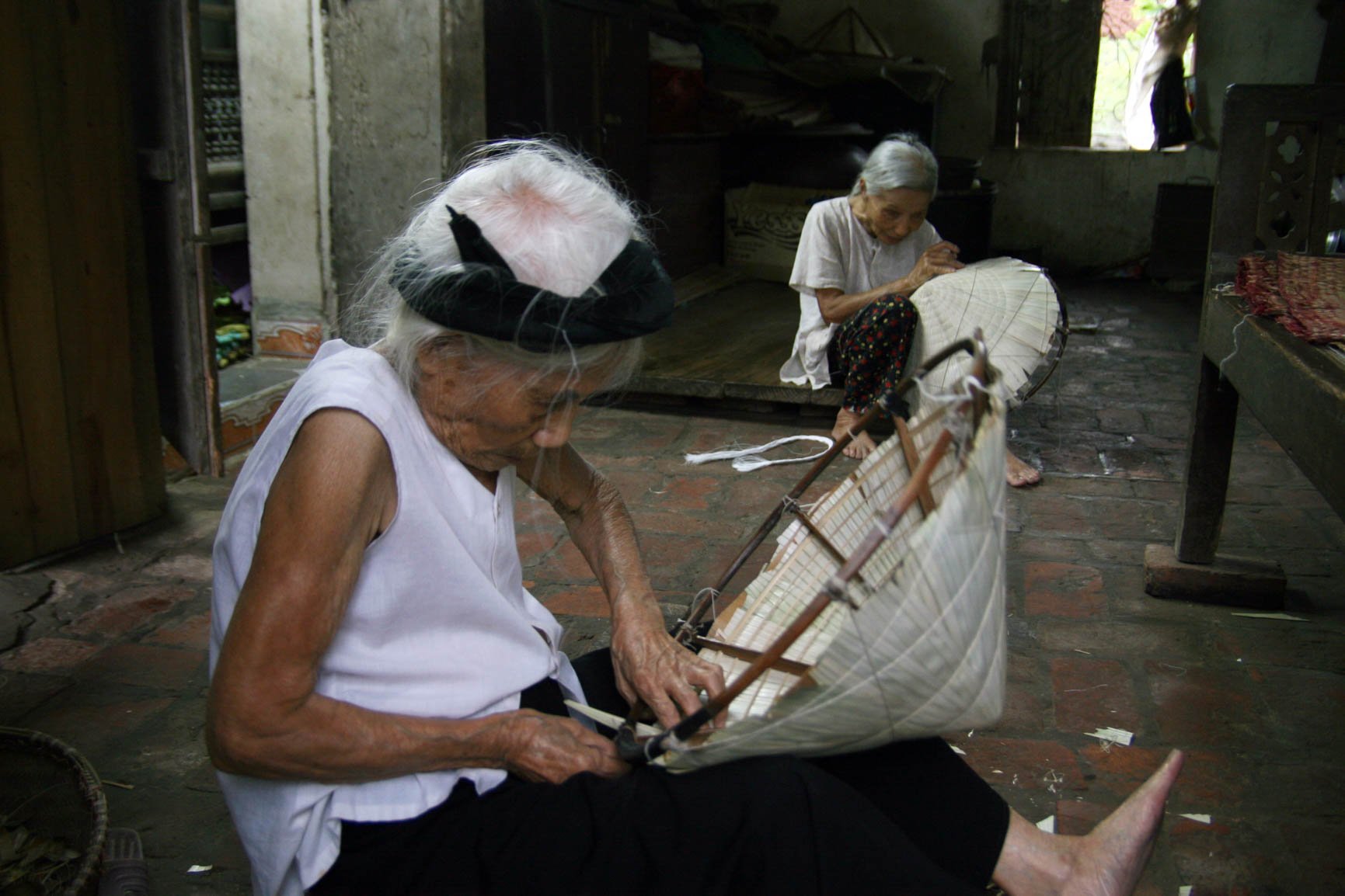 Bức ảnh xúc động được tác giả Lê Bích ghi lại tại làng Chuông (Thanh Oai). Trong ảnh là người mẹ 98 tuổi đang ngồi làm nón cùng con gái 78 tuổi bị mù lòa.