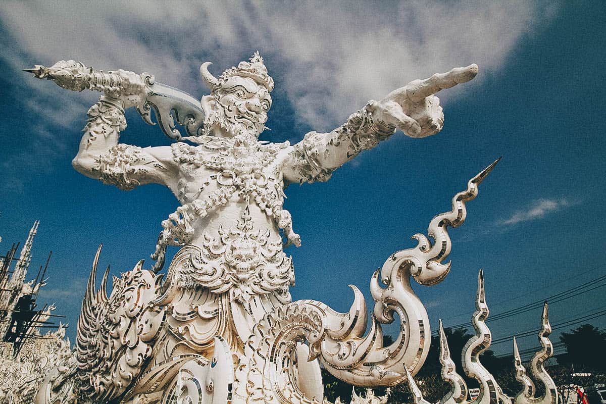 Ngoài tên gọi chính là Wat Rong Khun thì người Việt mình còn gọi là Chùa trắng Thái Lan bởi toàn bộ công trình có màu trắng. Được kết hợp với lối kiến trúc chùa cổ điển của Thái và phong cách siêu thực, bạn sẽ rất ngỡ ngàng khi chiêm ngưỡng một thiết kế độc đáo đến như vậy. Bước vào ngôi chùa, quan sát xung quanh, bạn cũng đủ choáng ngợp với vẻ đẹp của màu trắng tinh khiết như có tuyết rơi hiện hữu ở khắp mọi nơi. Bạn có thể thấy xung quanh ngôi chùa chính là một công viên có hồ cá cảnh và những tác phẩm điêu khắc tuyệt đẹp màu trắng. Bạn cũng sẽ ngạc nhiên là tại sao những chạm trổ và điêu khắc lại có thể tinh xảo đến như vậy, chỉ đứng ngắm nhìn hoài từ công trình này công trình khác mãi không biết chán.