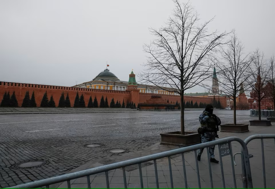 Một nhân viên thực thi pháp luật đứng gác ở Quảng trường Đỏ, nơi bị đóng cửa do các biện pháp an ninh được tăng cường, khi quốc kỳ Nga tung bay ở vị trí giữa cột trên mái vòm của tòa nhà Thượng viện Điện Kremlin trong ngày để tang - Ảnh: REUTERS/Shamil Zhumatov