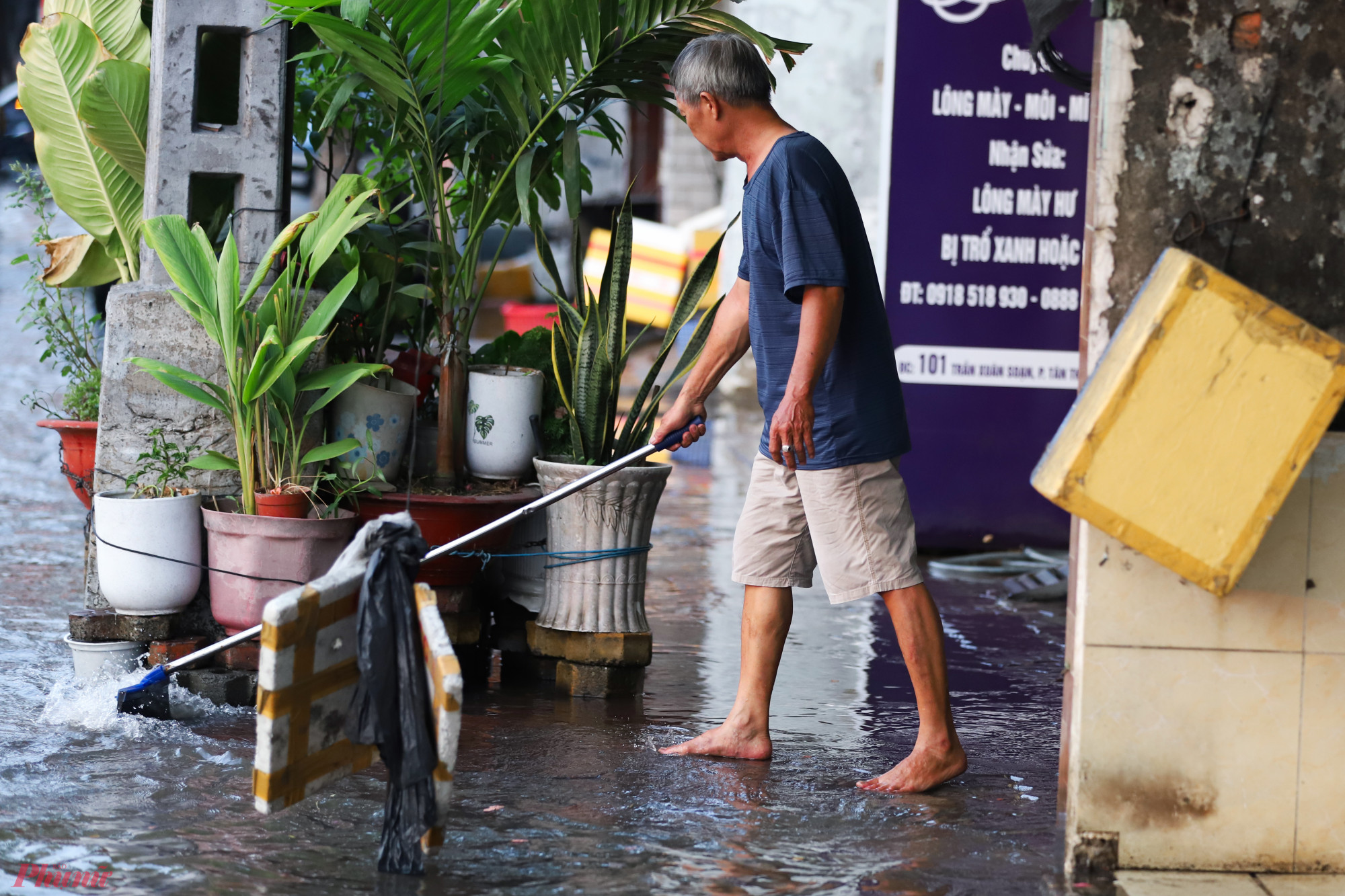 Người dân sống trên đường Trần Xuân Soạn phải dùng cây lau nhà ủi nước để tránh tràn vào nhà.