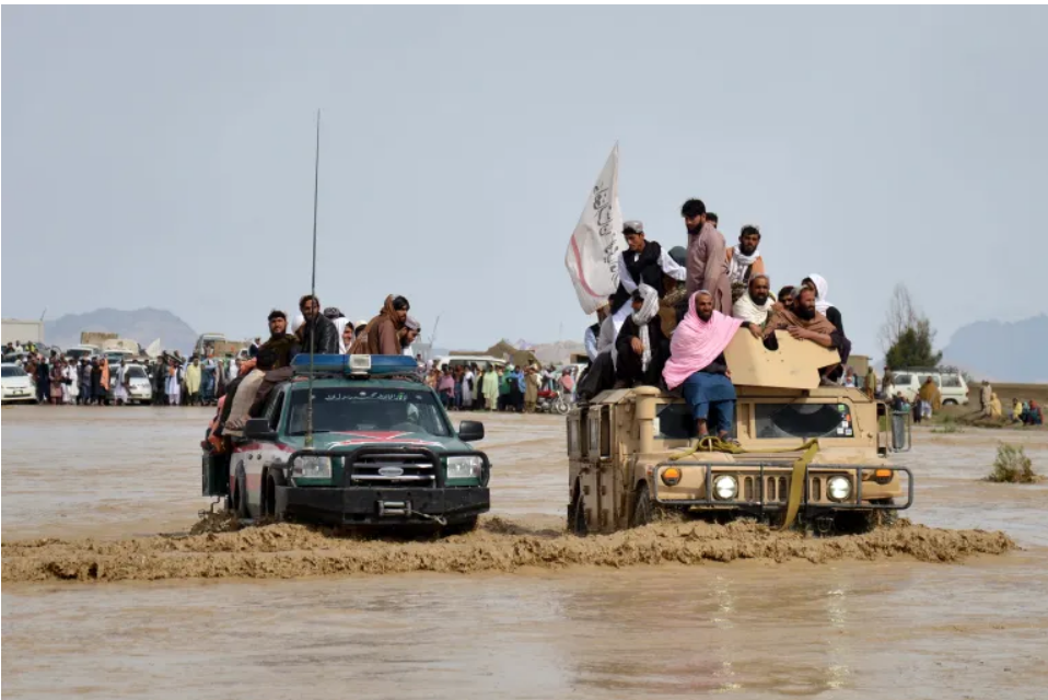 Những người đàn ông Afghanistan ngồi trên xe quân sự khi họ băng qua khu vực ngập lụt ở tỉnh Kandahar - Ảnh: AFP