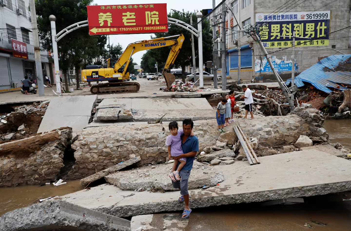 Người đàn ông bế đứa trẻ đi qua cây cầu bị hỏng sau những trận mưa lũ do tàn dư của cơn bão Doksuri quét qua vùng Trác Châu, tỉnh Hà Bắc, Trung Quốc ngày 7/8/2023 — Ảnh: Reuters