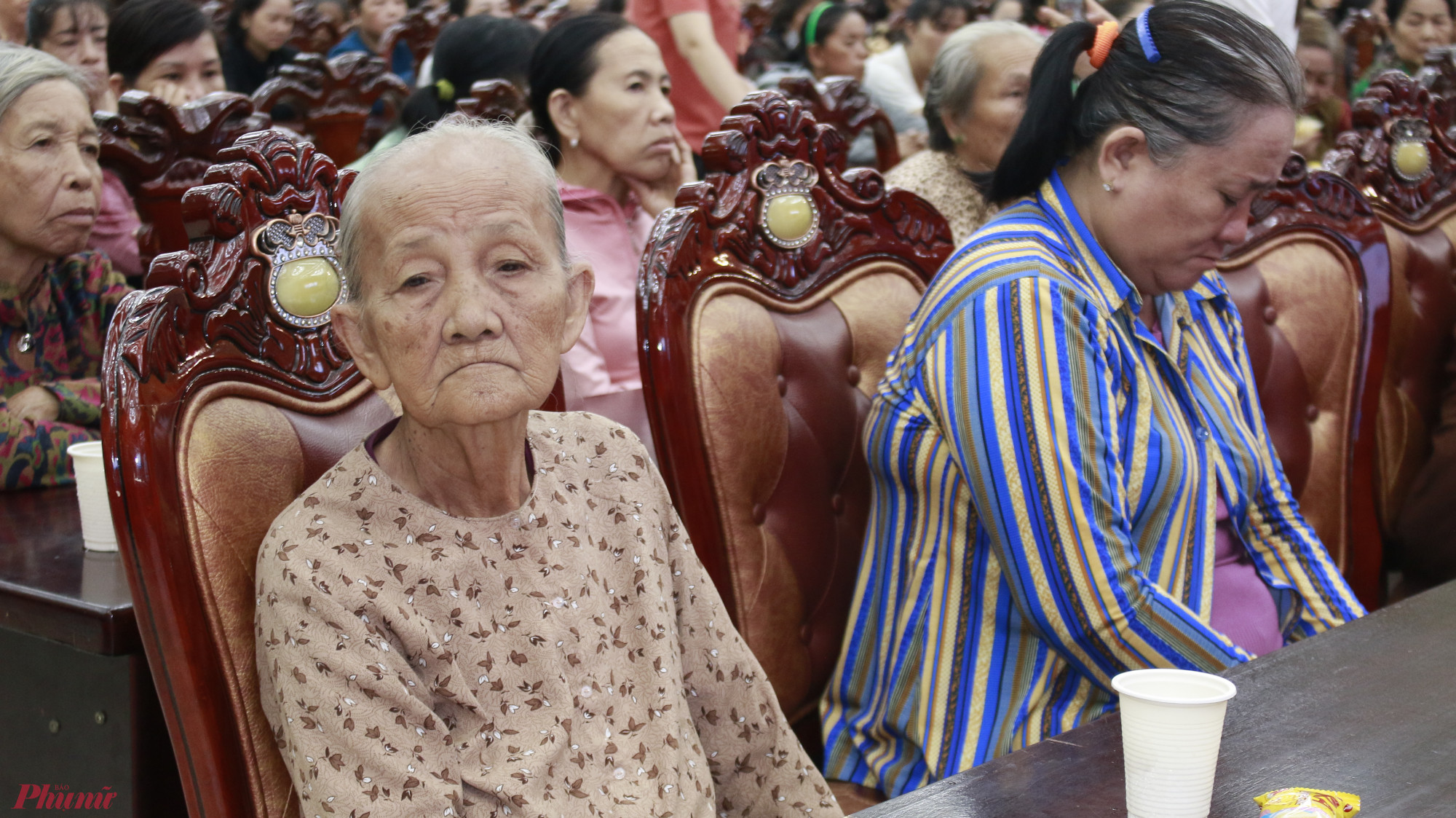 Bà Lê Thị Của (82 tuổi, ấp 4, xã Đa Phước, huyện Bình Chánh) ngồi lặng lẽ chờ đợi để nhận số tiền hỗ trợ. Bà Của tâm sự: 'Tôi buôn bán cháo lòng ven đường hơn 40 năm, nhưng cuộc sống vẫn không dư dả gì. Kinh tế khó khăn, bán được ngày nào thì ăn ngày nấy. Giờ đây, được hỗ trợ số tiền này, tôi sẽ dùng để mua thêm bàn, ghế và chén bát để phục vụ việc buôn bán.'