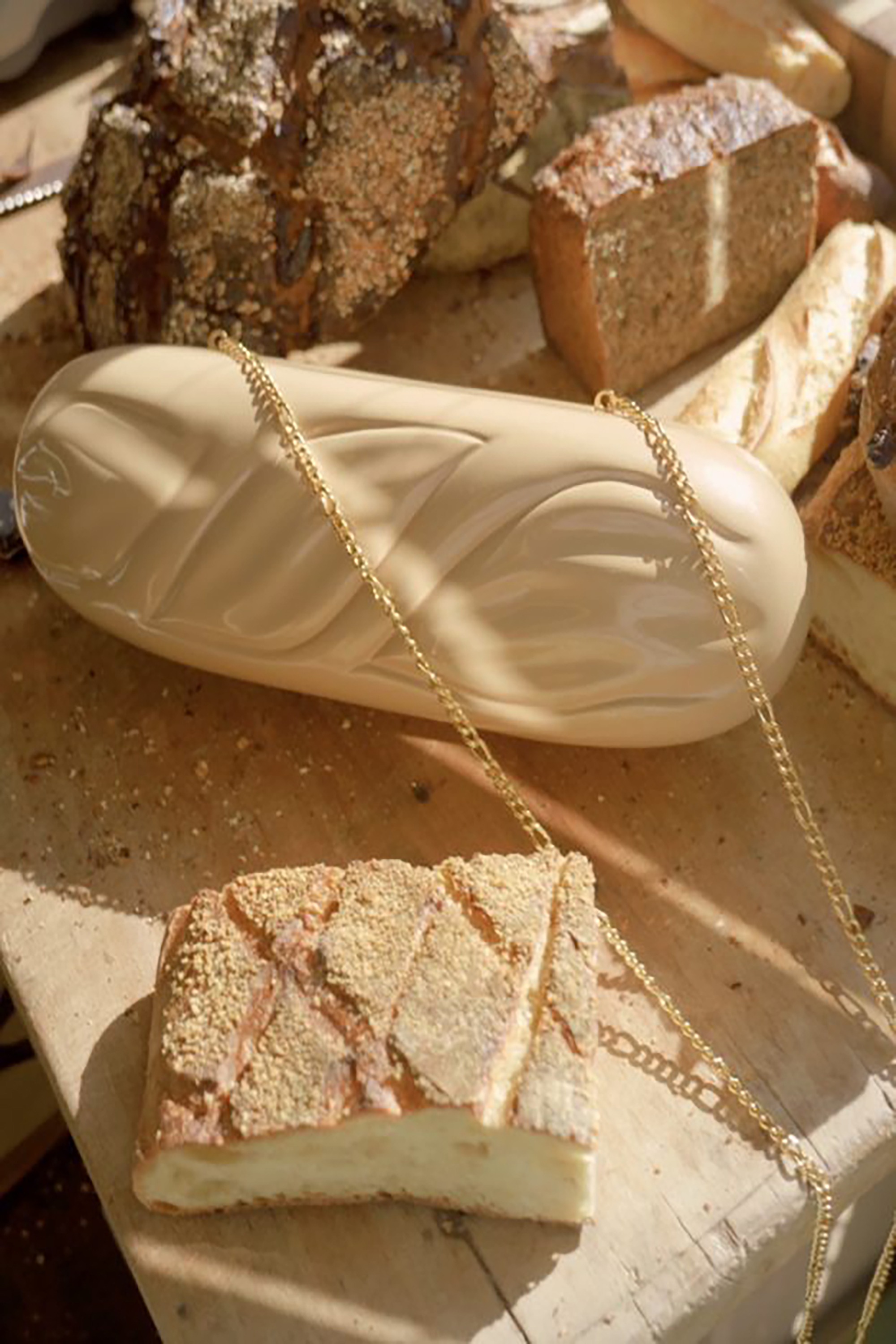 một chiếc túi cầm tay, có hình dáng giống như bánh mì baguette của Pháp, được làm bằng gỗ keo và có thể đeo trên vai nhờ dây xích kim loại vàng.