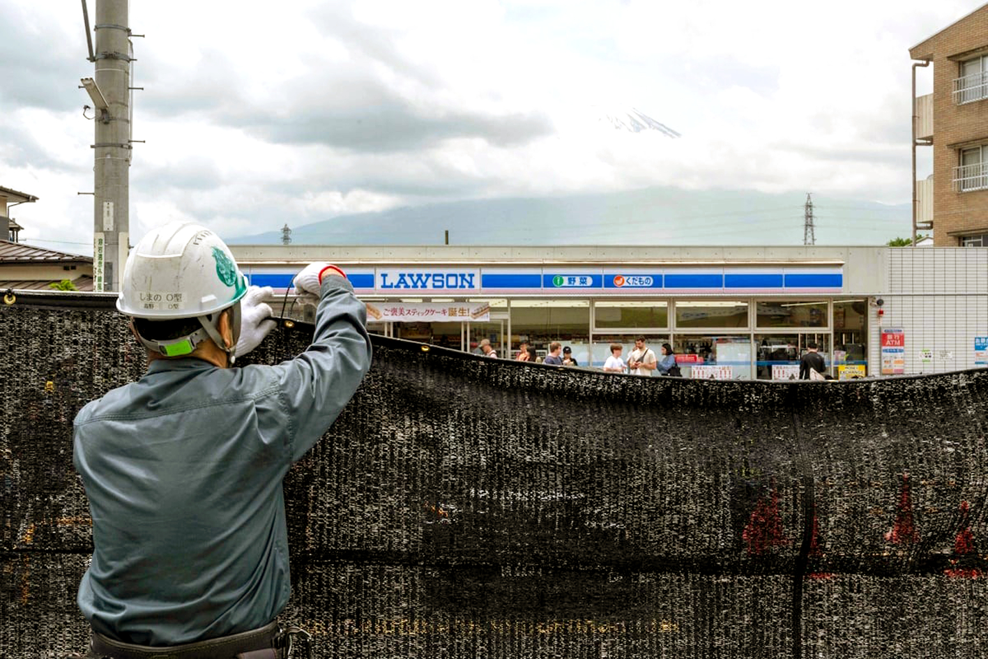 Một công nhân lắp đặt rào chắn bằng lưới để chặn tầm nhìn ra núi Phú Sĩ (Nhật Bản) từ một cửa hàng tiện lợi ở tỉnh Yamanashi - Nguồn ảnh: AFP