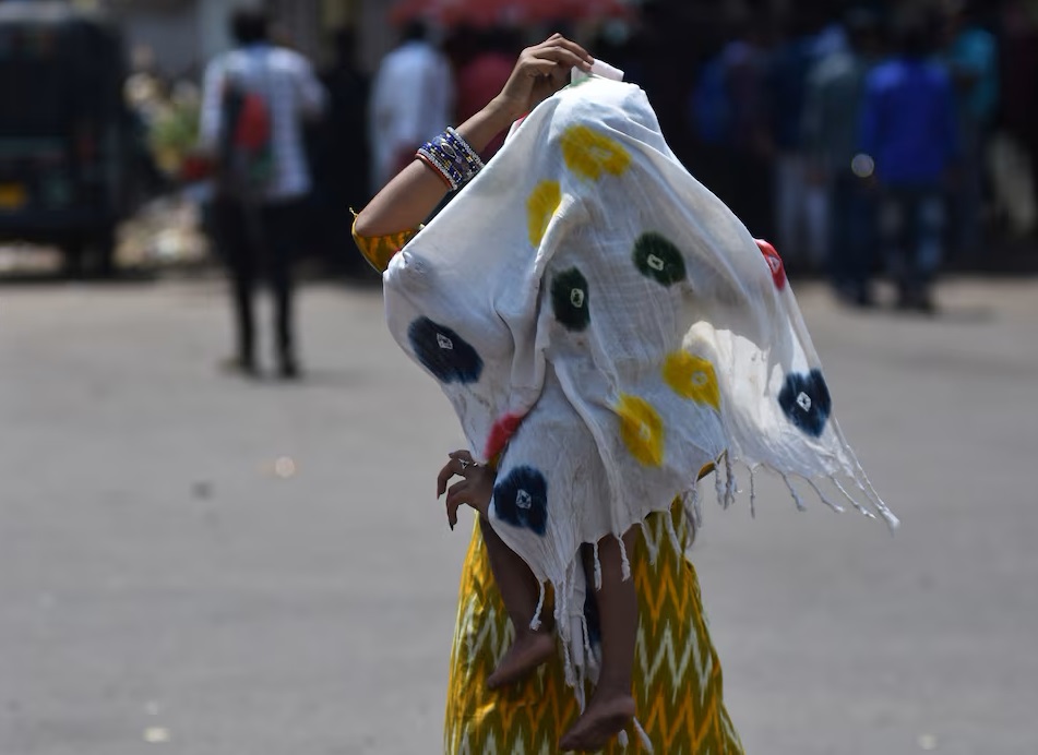 Một người phụ nữ che con mình bằng một chiếc khăn để bảo vệ đứa trẻ khỏi cái nóng trên đường ở Bhubaneswar, Ấn Độ, ngày 3/5/2024 - Ảnh: REUTERS/Stringer