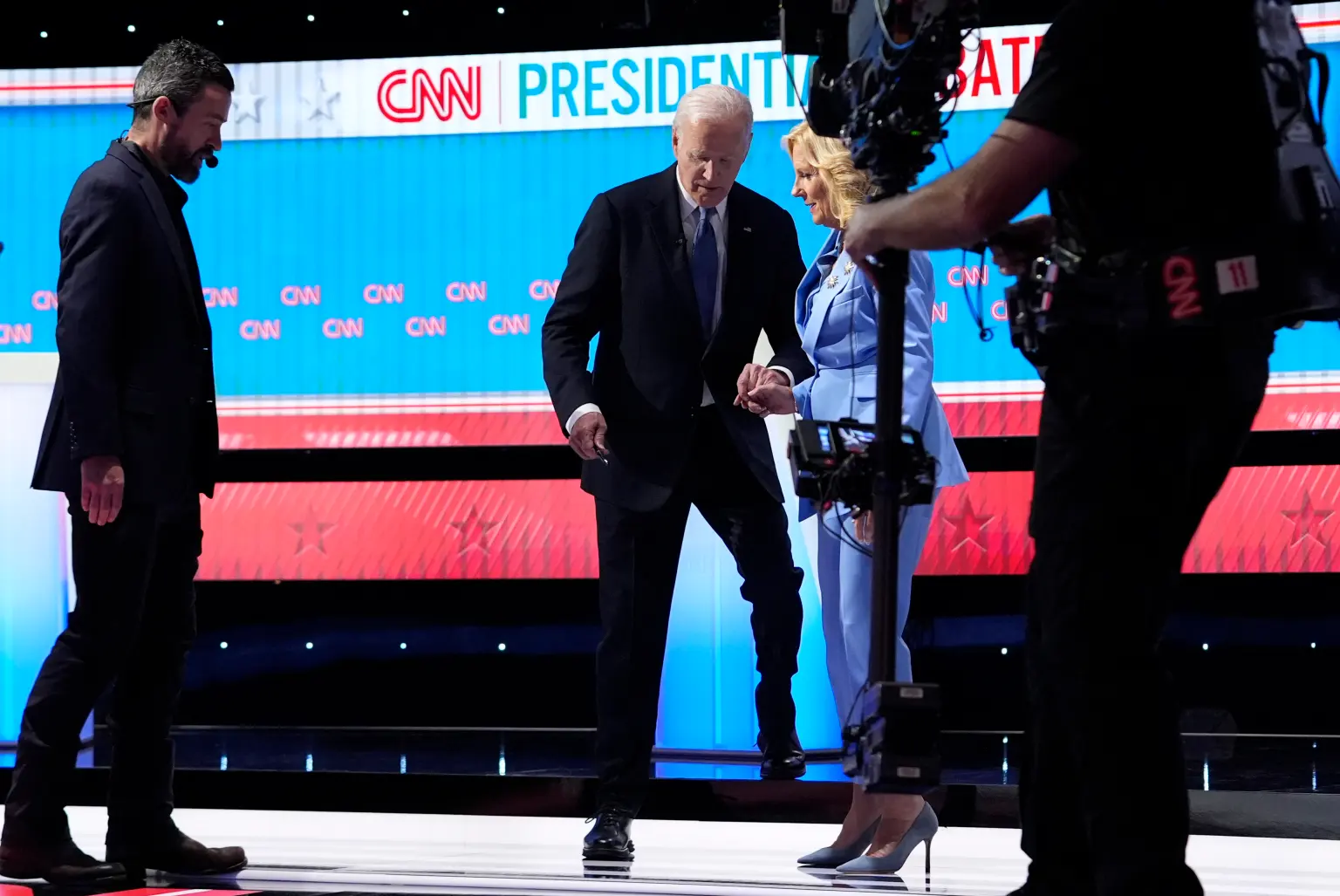 Tổng thống Joe Biden chậm rãi bước xuống bậc thềm sân khấu trong khi nắm chặt tay vợ vào ngày 27/6/2024 - Ảnh: AP