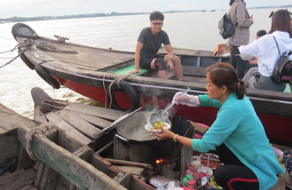 Một ghe bán bún cá, món ăn được coi là đặc sản của vùng đất Long Xuyên. Phía xa xa là cầu Vàm Cống bắc qua sông Hậu.