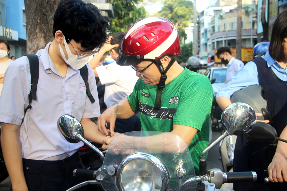 Anh Trần Hải (ngụ quận Tân Bình) cẩn thận  đeo đồng hồ vào tay con trai và nhắc con  canh thời gian để làm bài trong kỳ thi vào Trường phổ thông Năng khiếu (Đại học Quốc gia TPHCM) năm 2024 - Ảnh: Nguyễn Loan