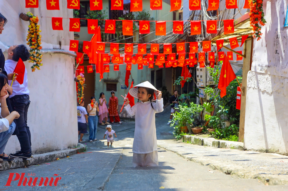 Những công dân nhí được cha mẹ đưa theo chụp ảnh với trang phục áo dài truyền thống, nón lá và cờ Tổ quốc cầm tay.