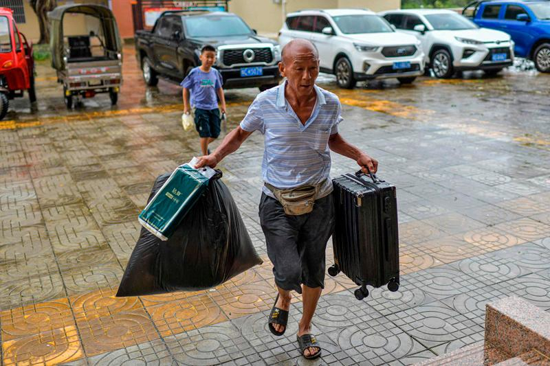 Một người dân địa phương mang thức ăn và hành lý đến nơi trú ẩn tạm thời tại một trường tiểu học trước khi Siêu bão Yagi dự kiến đổ bộ vào thành phố Văn Xương, tỉnh Hải Nam - Ảnh: CNS / AFP