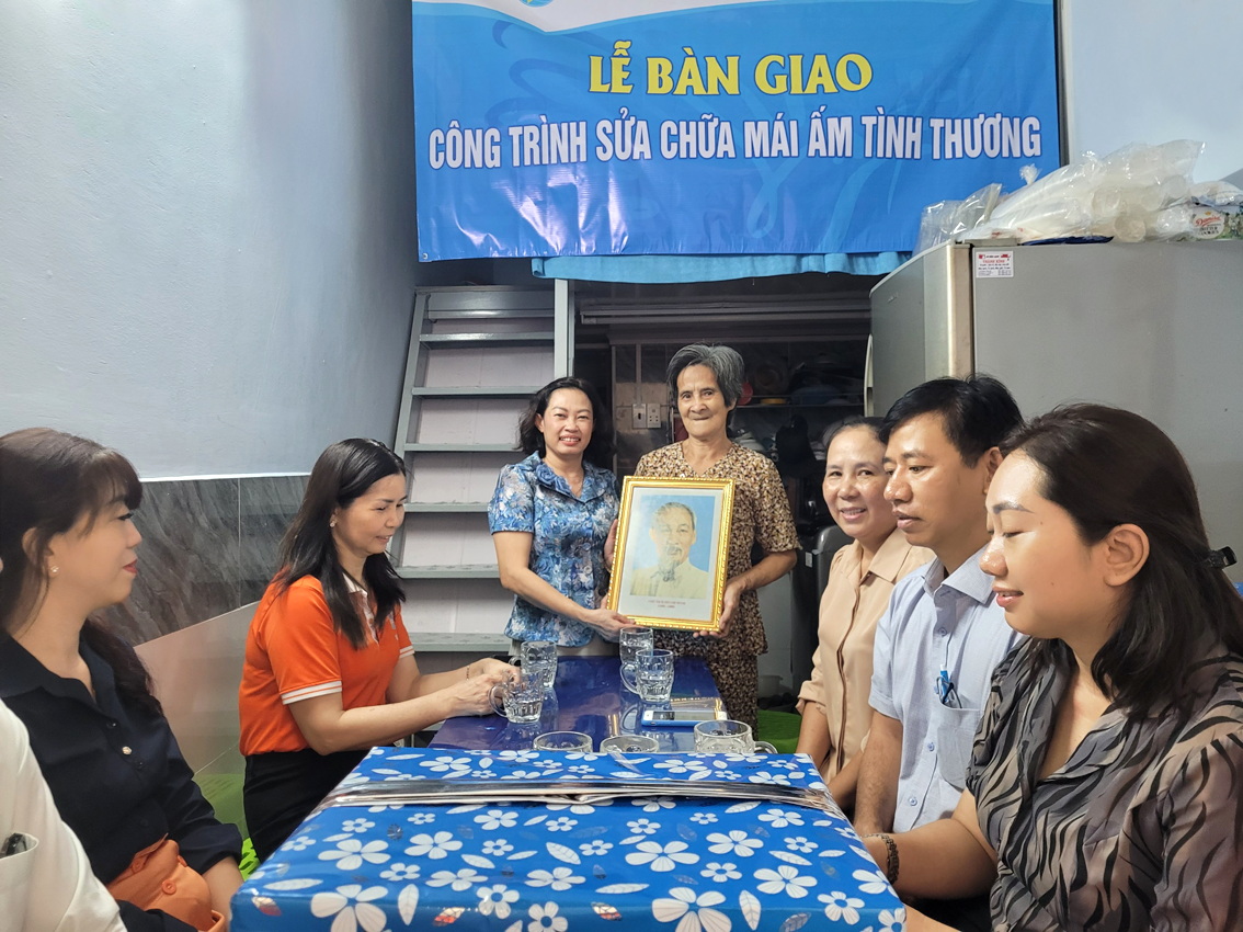 Bà Nguyễn Thùy Trinh (đứng, bên trái) tặng ảnh Bác Hồ cho bà Bùi Thị Hường trong ngày bàn giao mái ấm