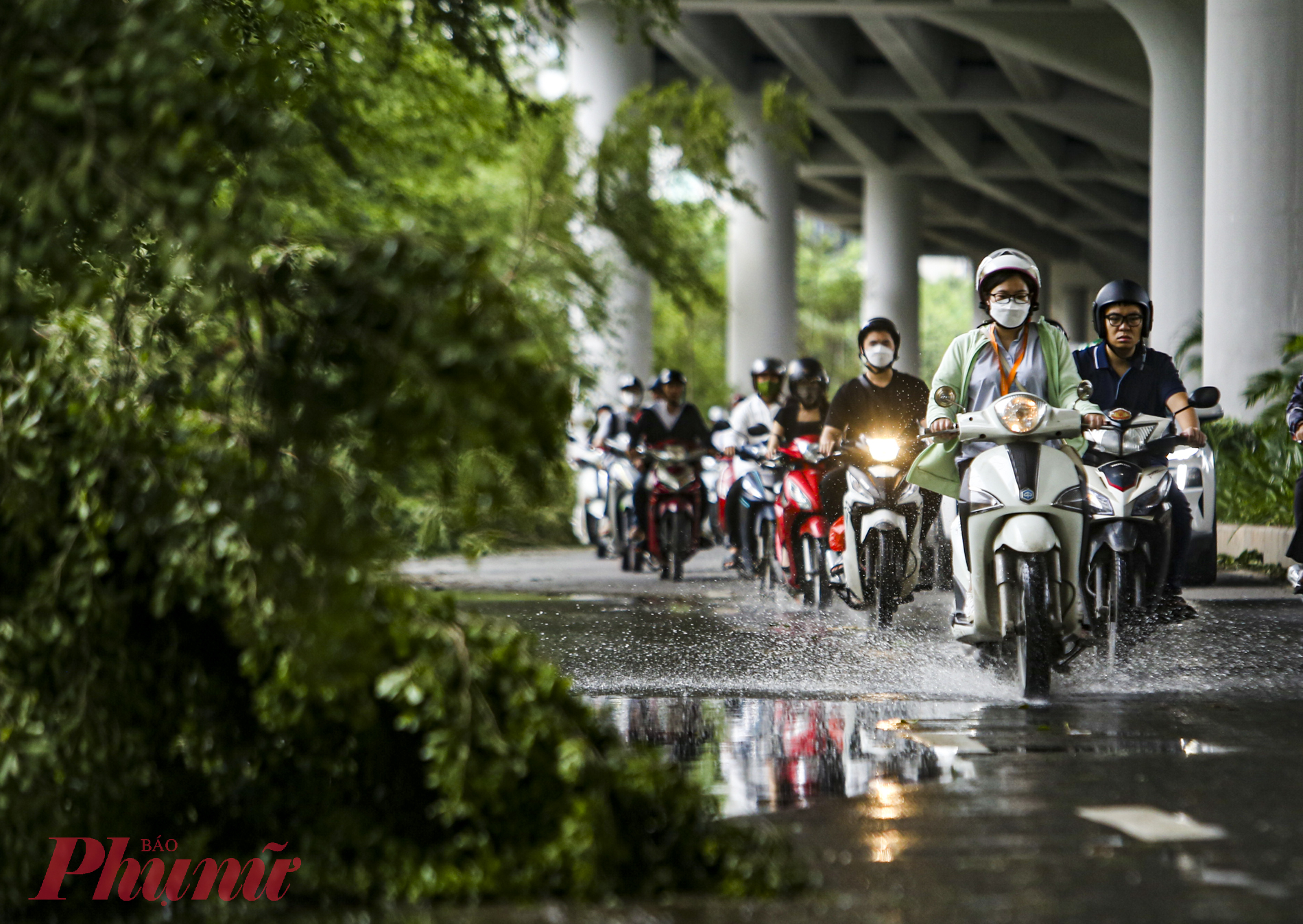 Một số điểm vẫn còn nước ứ đọng, mặt đường trơn trượt, phía trước là hàng cây đổ gục xuống lòng đường.