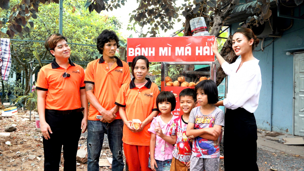 Đoàn Văn Minh Nhựt (bìa trái) và hoa hậu Bùi Xuân Hạnh (bìa phải) tặng xe bán bánh mì cho gia đình có hoàn cảnh khó khăn ở quận 7, TPHCM