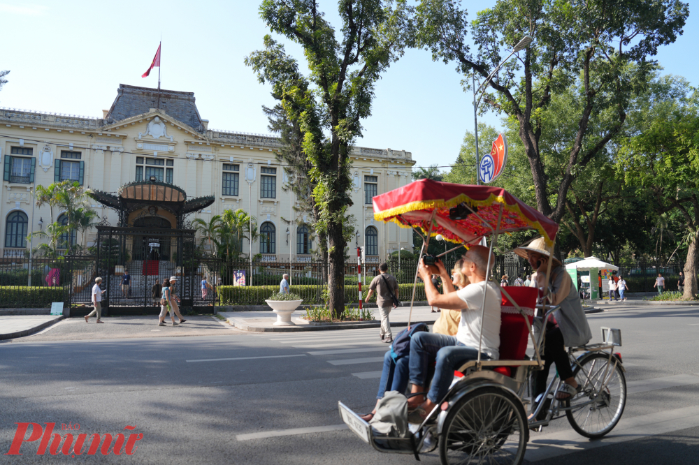   Du khách nước ngoài thích thú ngồi xích lô chụp ảnh tòa nhà Bắc Bộ Phủ.