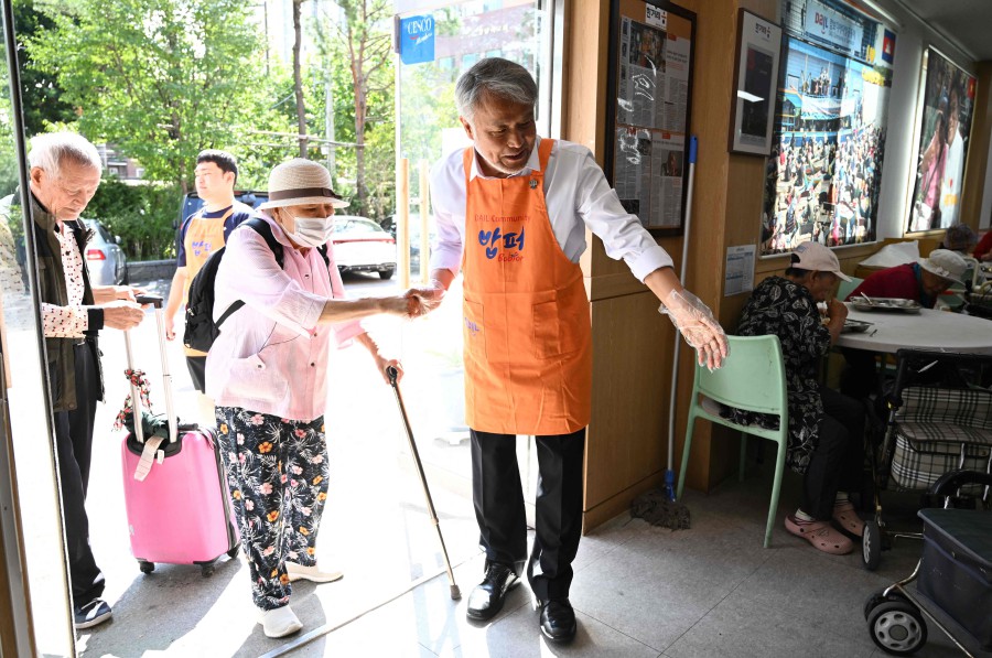 Ông Cho đang chào đón một phụ nữ cao tuổi đến nhận bữa ăn miễn phí tại trung tâm - Ảnh: AFP