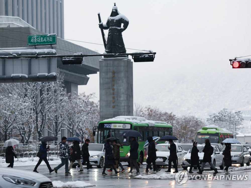 Mọi người đi bộ qua Quảng trường Gwanghwamun ở Seoul vào ngày 28/11 giữa màn tuyết rơi dày  - Ảnh: Yonhap