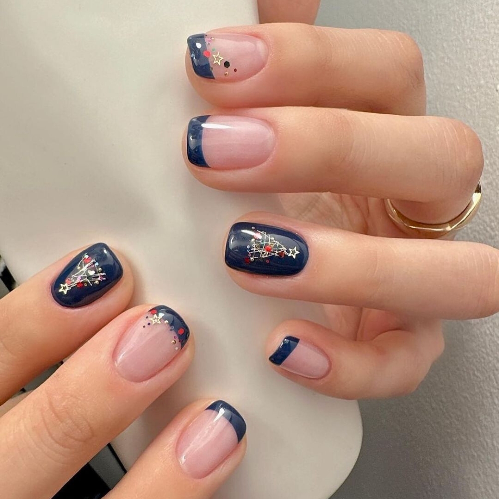 Nail sắc xanh navy: Sự đối lập hoàn hảo giữa sắc xanh navy trầm và họa tiết cây thông Noel rực rỡ đã tạo nên mẫu nail cá tính và đậm chất Giáng Sinh. Với thiết kế French tip hiện đại và chi tiết ánh sao nhỏ ở đầu móng, kiểu nail này mang đến vẻ đẹp vừa cổ điển vừa phá cách, khiến đôi tay bạn như bừng sáng giữa đêm đông.