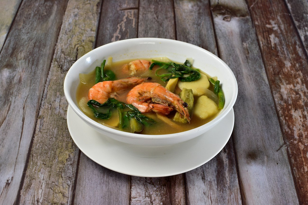 Sinigang là món canh chua truyền thống của Philippines, nổi bật với vị chua đậm đà nhờ me chín hoặc các nguyên liệu tạo vị chua khác như calamansi hoặc xoài xanh. Món này thường nấu cùng thịt (như thịt heo, bò, gà) hoặc hải sản, kèm rau củ như đậu bắp, cải thảo, cà chua, và củ môn. Sinigang có hương vị chua thanh, thơm ngon, thường được ăn kèm cơm trắng. Đây là món ăn đặc trưng trong ẩm thực Philippines, phù hợp với mọi bữa ăn.