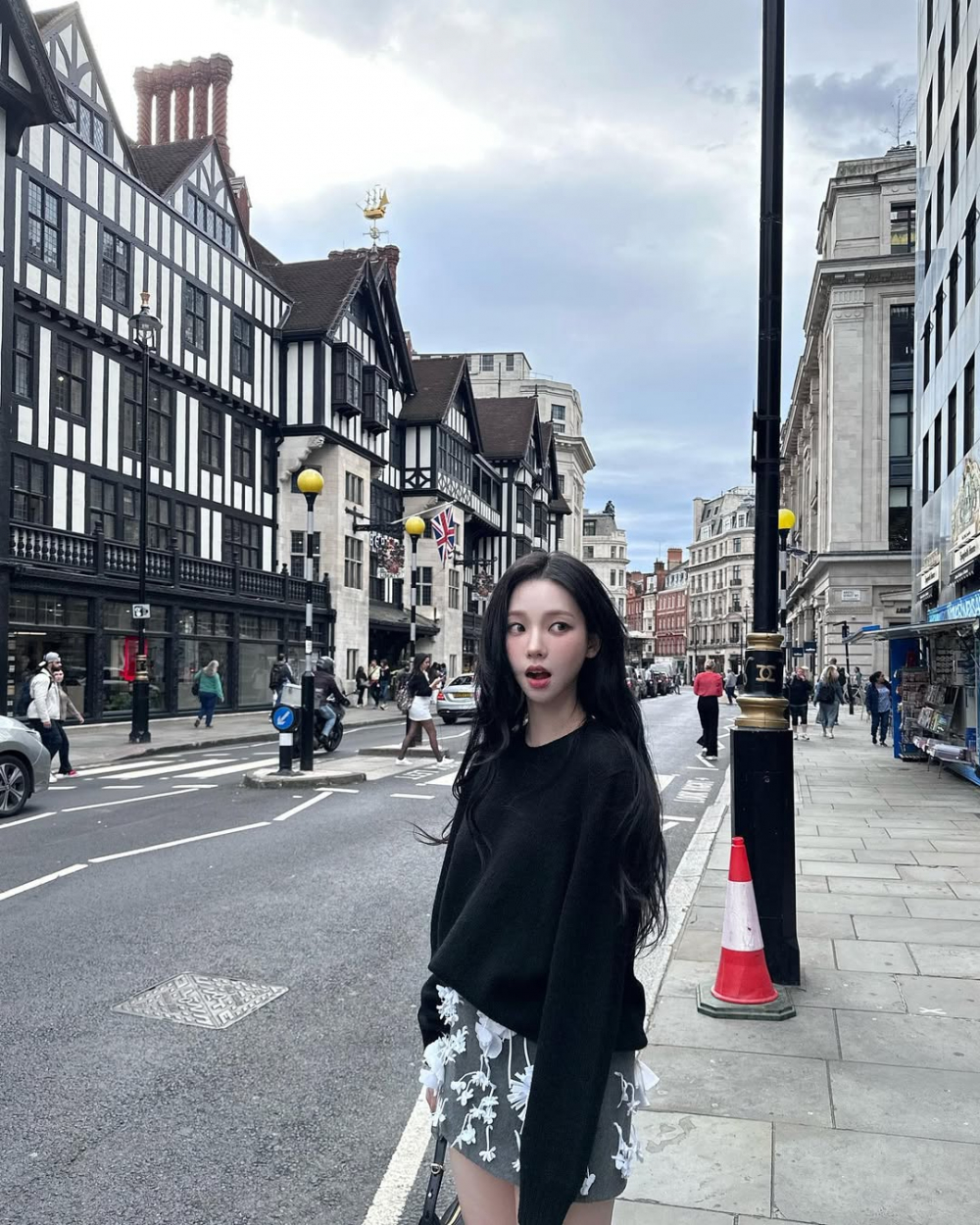 Tại London, Karina tiếp tục chứng minh gu thời trang tinh tế của mình với sự kết hợp giữa áo len đen đơn giản và chân váy ngắn họa tiết hoa 3D nổi bật. Dù chỉ xoay quanh hai tông màu đen và trắng, set đồ của cô vẫn thu hút mọi ánh nhìn nhờ thiết kế chân váy độc đáo, mang lại vẻ trẻ trung và “hack” chiều cao đáng kể. Karina khéo léo giữ sự tinh tế cho outfit bằng cách chọn giày và túi xách tông màu trung tính, tạo nên tổng thể hài hòa mà không mất đi nét hiện đại.