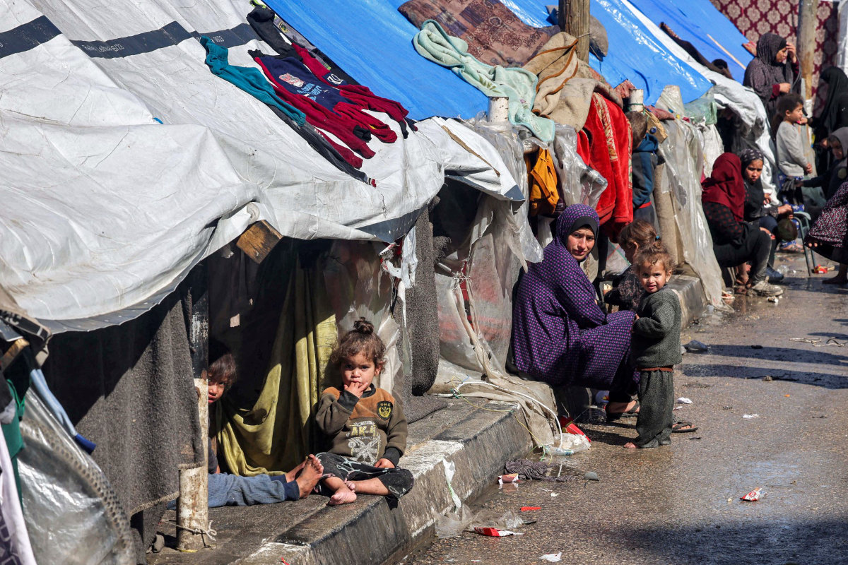 Một phụ nữ và trẻ em ngồi bên ngoài lều trú ẩn cho người Palestine phải di dời ở Rafah, phía nam Dải Gaza vào ngày 8 tháng 2 năm 2024, trong bối cảnh cuộc xung đột đang diễn ra giữa Israel và nhóm chiến binh Hamas của Palestine. (Tệp AFP)