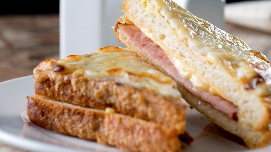 Croque-monsieur Theo Larousse, loại bánh sandwich nóng cổ điển của Pháp này bao gồm một lát giăm bông mỏng và phô mai tan chảy kẹp giữa hai lát bánh mì. Món đầu tiên xuất hiện trên thực đơn của người Paris vào năm 1910, và một số người cho rằng nó được phát minh ra một cách tình cờ, khi những công nhân Pháp để bữa trưa của họ gần một lò sưởi nóng, chỉ để quay lại sau đó và phát hiện ra rằng phô mai trong bánh sandwich của họ đã tan chảy.  Nếu bạn muốn nếm thử một chiếc croque đích thực, phô mai phải là Gruyere (trộn với bechamel để có được nước sốt Mornay) và toàn bộ chiếc bánh sandwich phải được xào trong bơ cho đến khi giòn và có màu vàng nâu. Croque-monsieur rất phổ biến đến nỗi tiểu thuyết gia nổi tiếng Proust thậm chí đã viết về nó trong kiệt tác năm 1918 của ông là In Search of Lost Time . 