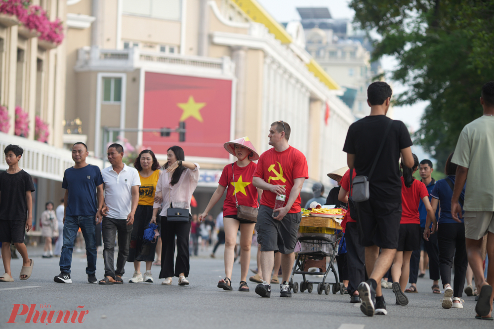 Những du khách nước ngoài thích thú mặc trên mình màu áo cờ đỏ sao vàng, cờ Đảng búa liềm, đội nón lá đi dạo trên phố đi bộ.