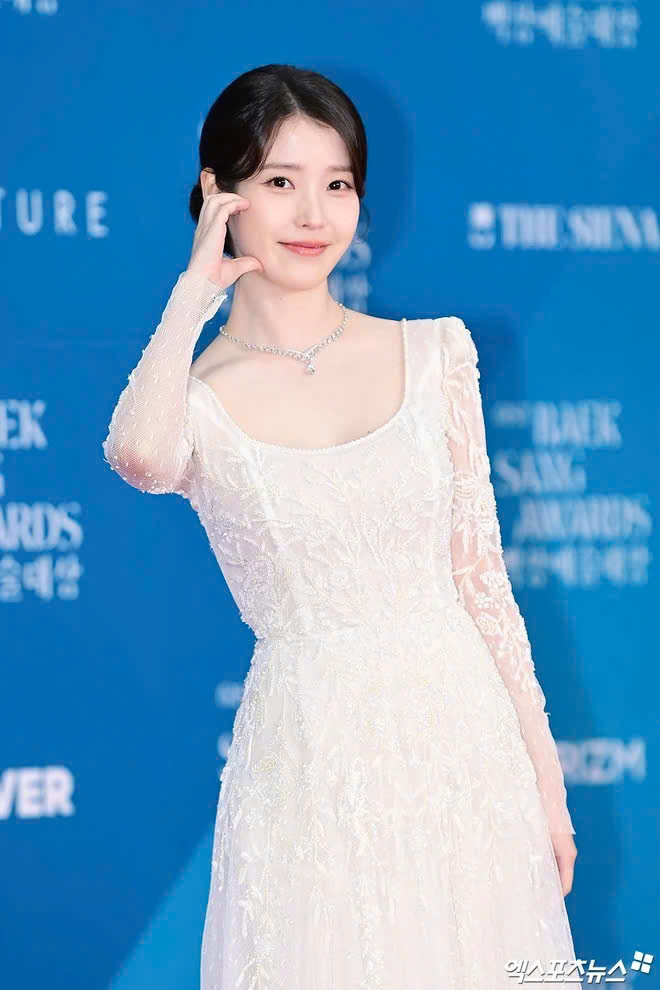 Em gái quốc dân IU sải bước trên thảm đỏ Baeksang trong chiếc váy trắng ren cổ vuông toát lên vẻ đẹp nền nã nhưng không kém phần gợi cảm. Cô nàng vừa góp mặt trong danh sách 40 ngôi sao quyền lực nhất Hàn Quốc, theo công bố của Forbes Korea.