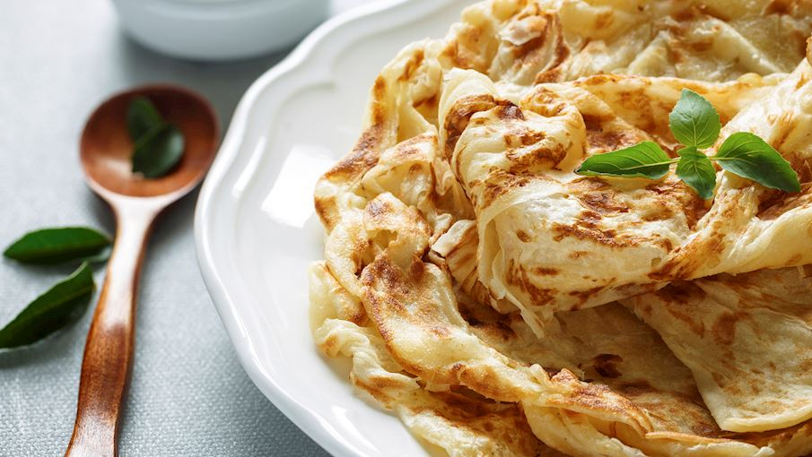 Roti canai là một món ăn sáng đặc trưng của Malaysia, có nguồn gốc từ cộng đồng người Ấn Độ di cư. Đây là loại bánh mì dẹt được làm từ bột mì, nước, bơ và đôi khi thêm trứng, sau đó nhào nặn kỹ và cán mỏng thành từng lớp. Khi nướng trên chảo phẳng, bánh có lớp vỏ giòn rụm nhưng bên trong lại mềm và dai. Roti canai thường được thưởng thức kèm với cà ri gà, cà ri dê hoặc dhal (món đậu hầm), tạo nên hương vị đậm đà, hấp dẫn. 