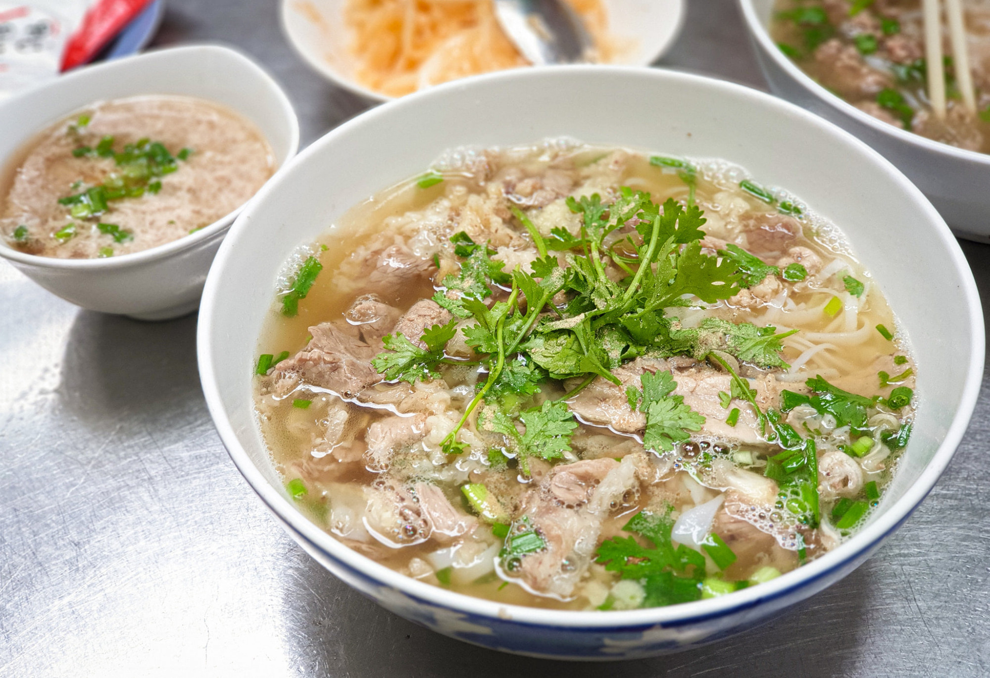 1. Phở Dậu – Hẻm 29 Nam Kỳ Khởi Nghĩa, Quận 3 Phở Dậu là một trong những quán phở Bắc hiếm hoi giữ được hương vị truyền thống giữa lòng Sài Gòn. Nước dùng ở đây đậm đà, ngọt thanh, được ninh kỹ từ xương ống, không quá béo nhưng rất đậm đà. Bánh phở mềm vừa phải, thịt bò thái lát mỏng, tươi ngon, đặc biệt phần tái và gân rất được lòng thực khách. Quán có không gian giản dị, hơi nhỏ nhưng sạch sẽ và ấm cúng. Giá một tô phở dao động từ 65.000 đến 100.000 đồng, hơi cao so với mặt bằng chung nhưng hoàn toàn xứng đáng với chất lượng. Google đánh giá quán 4.0 sao, phản ánh sự yêu thích của nhiều thực khách. Nếu bạn muốn thưởng thức phở Bắc chuẩn vị, Phở Dậu là điểm đến không thể bỏ qua.