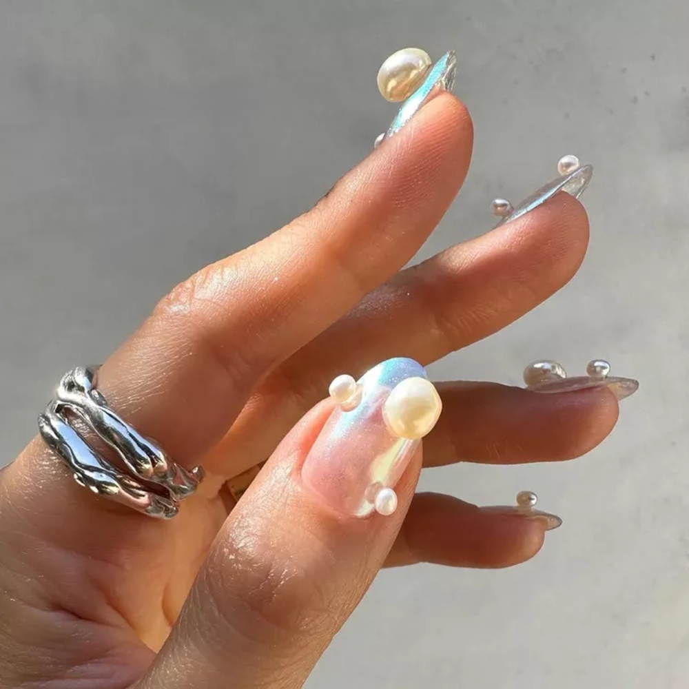 Mẫu nail đính ngọc trai: Với hiệu ứng bắt sáng huyền ảo, mẫu nail ngọc trai sẽ là gợi ý lý tưởng cho kỳ nghỉ mùa hè giúp các nàng trở nên thanh lịch, đẹp nhẹ nhàng mà vẫn đầy cuốn hút. Chỉ với vài viên ngọc trai được đính lên phần móng, đôi tay bạn sẽ toát lên vẻ đẹp sang trọng và thanh thoát. Từ những giây phút thong dong bên bãi biển cho buổi tiệc thưởng thức ly cocktail dưới ánh hoàng hôn trên biển, kiểu móng này sẽ tôn lên khí chất quyến rũ cho chị em.