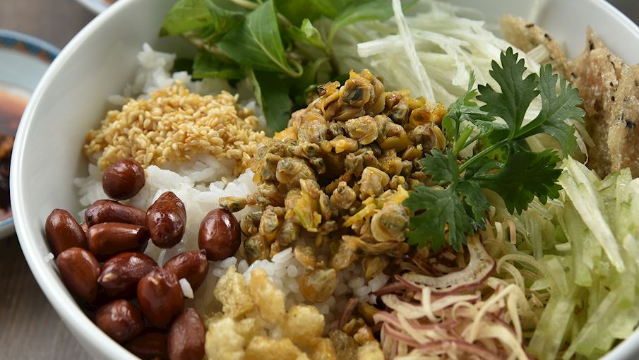 Cơm hến là món ăn đặc sản nổi tiếng của Huế, mang đậm hương vị dân dã nhưng đầy tinh tế. Món ăn gồm cơm nguội hoặc để nguội tự nhiên, ăn kèm hến xào, tóp mỡ, lạc rang, rau thơm, khế chua, bắp chuối thái mỏng và mắm ruốc Huế. Một bát nước luộc hến nóng đậm đà thường được dọn kèm để chan vào cơm theo sở thích. Khi ăn, thực khách trộn đều các thành phần, thưởng thức vị mặn mà, chua nhẹ, bùi béo hài hòa. Cơm hến thường được ăn kèm bánh tráng nướng giòn, là lựa chọn độc đáo không thể bỏ qua khi đến Huế.