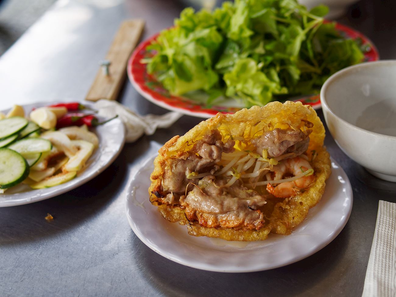 Bánh khoái là món bánh chiên giòn đặc trưng xứ Huế, thường được làm từ bột gạo pha với trứng, nước và gia vị. Nhân bánh gồm tôm, thịt, nấm, giá đỗ, cà rốt và hành lá, được chiên đến khi vàng giòn hấp dẫn. Điểm đặc biệt tạo nên hương vị riêng của bánh khoái là nước chấm béo bùi làm từ gan heo, đậu phộng, mè và bơ đậu phộng. Khi ăn, bánh được cuốn cùng rau sống như tía tô, xà lách, húng quế. Món ăn này thường được thưởng thức vào những ngày se lạnh, mang lại cảm giác ấm áp và đậm đà.