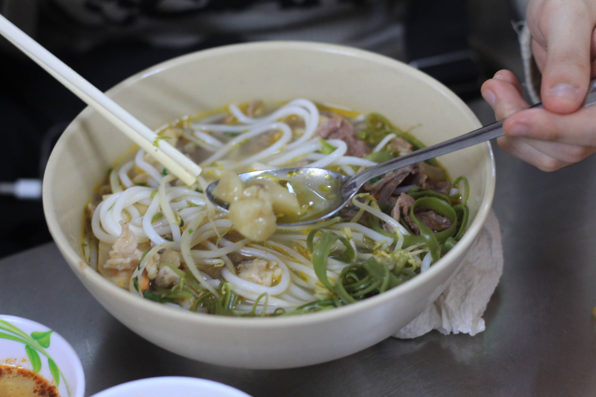 1. Bún bò Huế Cô Như – mỡ nổi đậm đà Nằm trong hẻm nhỏ trên đường Võ Văn Tần, quán Cô Như nhìn đơn sơ nhưng lúc nào cũng tấp nập khách. Tô bún ở đây “gây nghiện” bởi nước dùng ngọt thanh từ xương bò, cay nhẹ và thơm nức mùi sả, nổi bật với lớp mỡ óng ánh trên mặt – đúng kiểu “mỡ nổi” trứ danh. Thịt nạm mềm, chả cua thơm, rau sống xanh giòn – mọi thứ hòa quyện hài hòa. Quán sạch sẽ, phục vụ nhanh, giá chỉ từ 50.000 đồng.