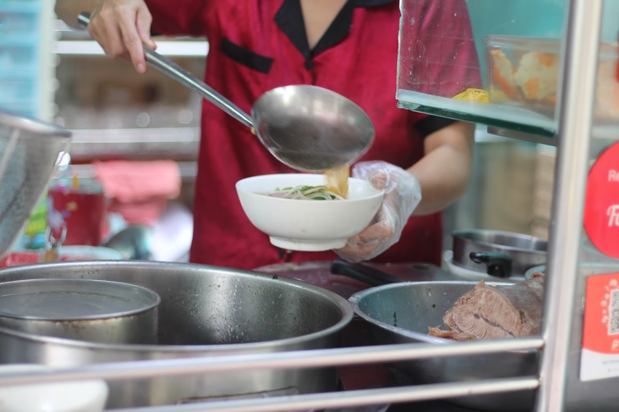 Chúng tôi đến quán bún bò Huế Út Mai (812/23 Trường Sa, Quận 3, TPHCM) theo lời giới thiệu của người bạn về quán bún bò ngon, chất, giá ổn. Tô bún bò hai người ăn mới hết ở đường Trường Sa Quán nằm trong một con hẻm nhỏ và cũng như nhiều nơi khác - trước quán là chiếc tủ kính đựng các nguyên liệu của món ăn, bên trong là vài chiếc bàn inox. Cảm giác sạch sẽ nhưng khá nhiều vật dụng khiến không gian như nhỏ hơn. Quán bún bò Huế nhưng thực đơn chia hẳn thành 17 món và giá đều từ 45.000 - 55.000 đồng. h Được bạn đảm bảo nên chúng tôi gọi hai tô thập cẩm đặc biệt (giá 55.000 đồng/tô) nhằm thử được tất cả thành phần mà quán có với bún bò. Bếp mở b Gian bếp mở khá thuận tiện để thực khách quan sát thao tác của người bán  h Chưa tới 5 phút, hai tô bún bò lần lượt dọn lên và điều khiến chúng tôi choáng ngợp chính là kích thước của tô bún cùng lượng thịt. Dù cùng gọi thập cẩm nhưng cậu bạn yêu cầu giò heo riêng, trong khi tô tôi là miếng sườn bò khủng với phần sụn bắt mắt.  Tô bún bò Huế đầy ắp thịt cùng miếng sườn bò khủng. Sườn bò có vẻ được xử lý khá kỹ trước khi chế biến nên gần không còn nặng mùi. Không chỉ vậy, sườn được nấu với thời gian khá chuẩn - phần sụn giòn, sần sật nhưng thịt không nhão, không rơi khi thưởng thức. Bún bò tại quán có nước dùng thanh, ngọt nhẹ do được hầm từ xương. Các loại thịt thà ăn kèm đều được xử lý và chế biến khéo léo để không để lại mùi lại làm bật hương, vị riêng của nguyên liệu mang đến cho tôi cảm giác không cần ăn kèm nước lèo, chỉ cần cho tôi chén mắm cay hay mắm ruốc, tôi đã có thể thưởng thức ngon la Bún bò tại quán có nước dùng thanh, ngọt nhẹ, do được hầm từ xương. Các loại thịt ăn kèm đều được xử lý và chế biến khéo léo, làm bật lên hương vị riêng của nguyên liệu. Theo chị Mai, chủ quán cũng là người đứng bán, hầu hết thành phần trong món bún bò do chị tự tay chọn nguyên liệu, xử lý và chế biến. Mỗi ngày, chị bán được vài chục ký thịt các loại. Chị kể mỗi ngày phải thức đến nửa đêm để nấu và chuẩn bị mọi thứ, nhưng sáng hôm sau vẫn phải dậy từ 4g30, chuẩn bị đến 7g30 mới có thể mở cửa đón khách. Nhiều lúc mệt quá, muốn nghỉ một bữa, nhưng nghĩ khách nhớ mình, đến quán, không gặp, lại cố, chị tâm sự.