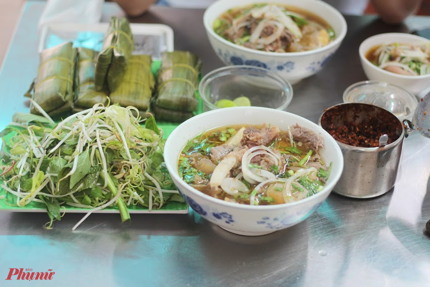 Chúng tôi đến quán bún bò Huế Út Mai (812/23 Trường Sa, Quận 3, TPHCM) theo lời giới thiệu của người bạn về quán bún bò ngon, chất, giá ổn. Tô bún bò hai người ăn mới hết ở đường Trường Sa Quán nằm trong một con hẻm nhỏ và cũng như nhiều nơi khác - trước quán là chiếc tủ kính đựng các nguyên liệu của món ăn, bên trong là vài chiếc bàn inox. Cảm giác sạch sẽ nhưng khá nhiều vật dụng khiến không gian như nhỏ hơn. Quán bún bò Huế nhưng thực đơn chia hẳn thành 17 món và giá đều từ 45.000 - 55.000 đồng. h Được bạn đảm bảo nên chúng tôi gọi hai tô thập cẩm đặc biệt (giá 55.000 đồng/tô) nhằm thử được tất cả thành phần mà quán có với bún bò. Bếp mở b Gian bếp mở khá thuận tiện để thực khách quan sát thao tác của người bán  h Chưa tới 5 phút, hai tô bún bò lần lượt dọn lên và điều khiến chúng tôi choáng ngợp chính là kích thước của tô bún cùng lượng thịt. Dù cùng gọi thập cẩm nhưng cậu bạn yêu cầu giò heo riêng, trong khi tô tôi là miếng sườn bò khủng với phần sụn bắt mắt.  Tô bún bò Huế đầy ắp thịt cùng miếng sườn bò khủng. Sườn bò có vẻ được xử lý khá kỹ trước khi chế biến nên gần không còn nặng mùi. Không chỉ vậy, sườn được nấu với thời gian khá chuẩn - phần sụn giòn, sần sật nhưng thịt không nhão, không rơi khi thưởng thức. Bún bò tại quán có nước dùng thanh, ngọt nhẹ do được hầm từ xương. Các loại thịt thà ăn kèm đều được xử lý và chế biến khéo léo để không để lại mùi lại làm bật hương, vị riêng của nguyên liệu mang đến cho tôi cảm giác không cần ăn kèm nước lèo, chỉ cần cho tôi chén mắm cay hay mắm ruốc, tôi đã có thể thưởng thức ngon la Bún bò tại quán có nước dùng thanh, ngọt nhẹ, do được hầm từ xương. Các loại thịt ăn kèm đều được xử lý và chế biến khéo léo, làm bật lên hương vị riêng của nguyên liệu. Theo chị Mai, chủ quán cũng là người đứng bán, hầu hết thành phần trong món bún bò do chị tự tay chọn nguyên liệu, xử lý và chế biến. Mỗi ngày, chị bán được vài chục ký thịt các loại. Chị kể mỗi ngày phải thức đến nửa đêm để nấu và chuẩn bị mọi thứ, nhưng sáng hôm sau vẫn phải dậy từ 4g30, chuẩn bị đến 7g30 mới có thể mở cửa đón khách. Nhiều lúc mệt quá, muốn nghỉ một bữa, nhưng nghĩ khách nhớ mình, đến quán, không gặp, lại cố, chị tâm sự.