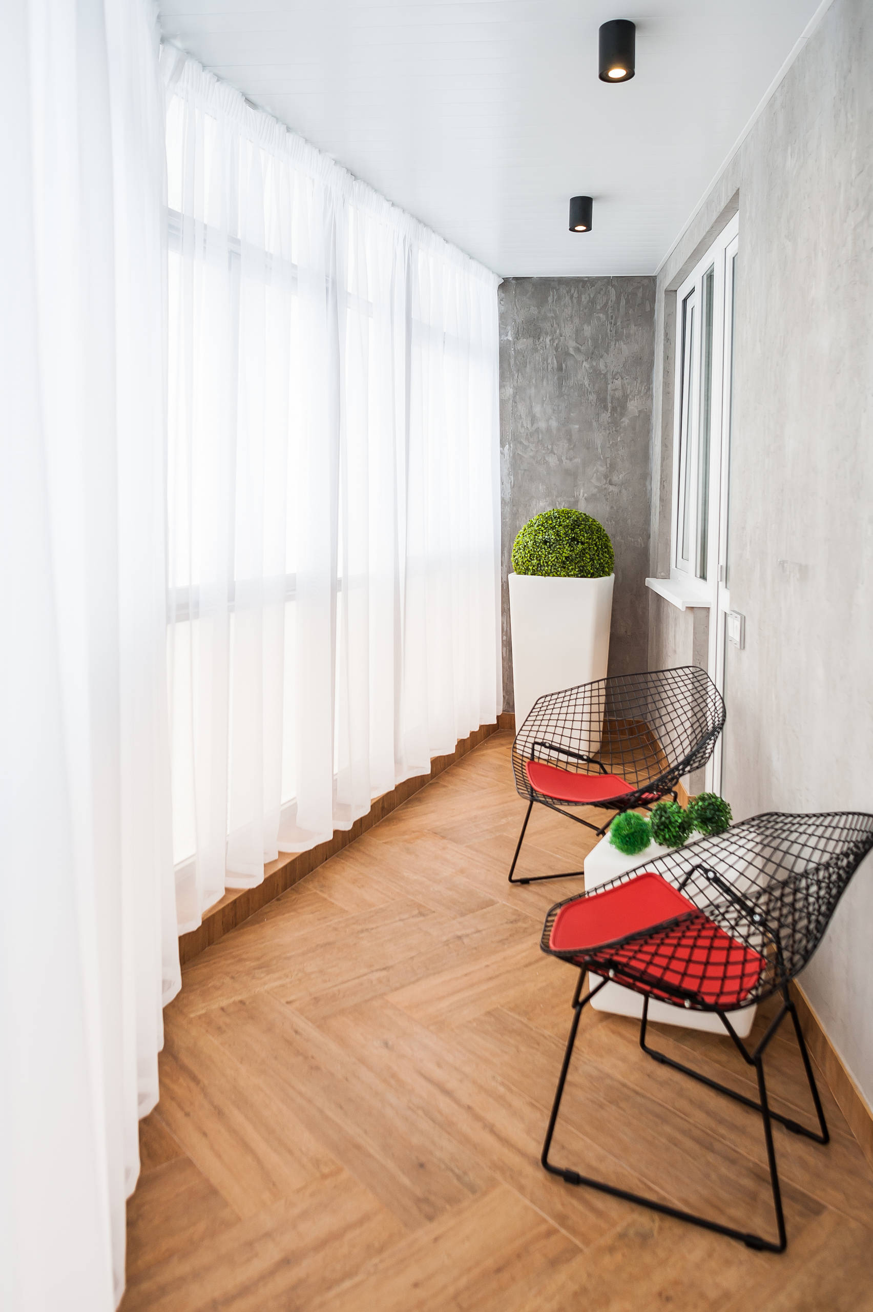 Ban công phòng tắm nắng Curtainsider có sàn gỗ: Đối với ban công phòng tắm nắng, nơi sử dụng rèm trắng để tạo sự riêng tư và kiểm soát ánh nắng mặt trời, gỗ sáng màu được ưu tiên làm vật liệu sàn. Những chiếc ghế trong phòng sử dụng sơn màu xám trên tường là ghế kim loại hiện đại.Houzz.com – Tín dụng |  © Insomnia