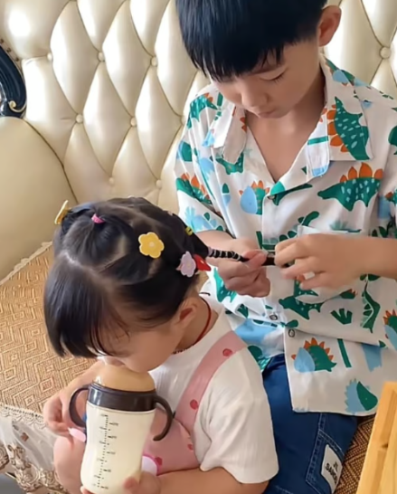 Trong khi anh trai cô tập trung vào việc tết, cô bé, thường được nhìn thấy nhấm nháp sữa từ bình, dường như thực sự thích sự chăm sóc chu đáo của anh ấy. Ảnh: Douyin
