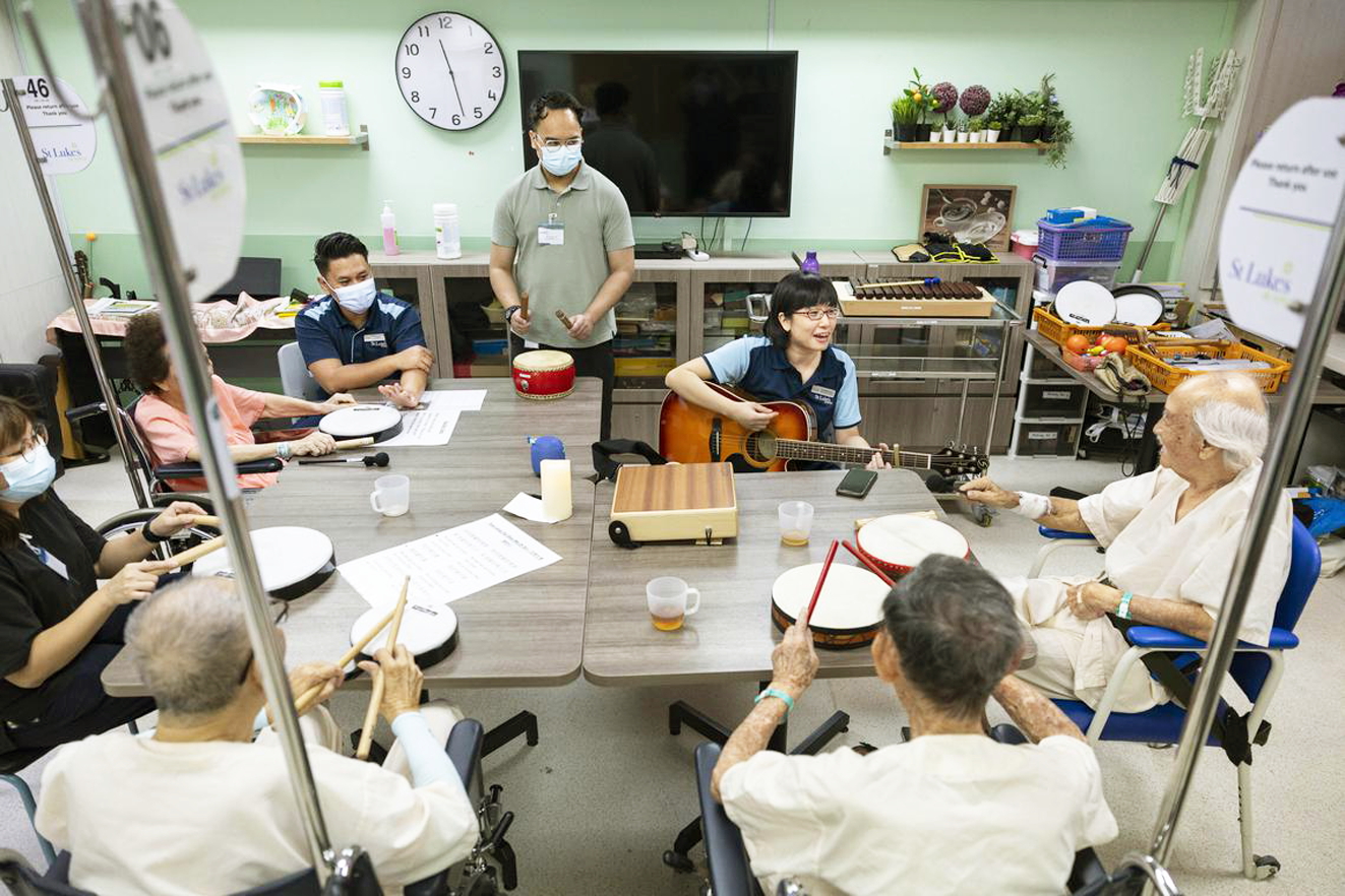 Bakti Khair (đứng) hỗ trợ chuyên gia trị liệu âm nhạc cao cấp Camellia Soon (chơi guitar) thực hiện buổi trị liệu âm nhạc với những bệnh nhân mất trí nhớ tại Bệnh viện St Luke (Singapore) - ẢNH: BRIAN TEO (Straits Times)