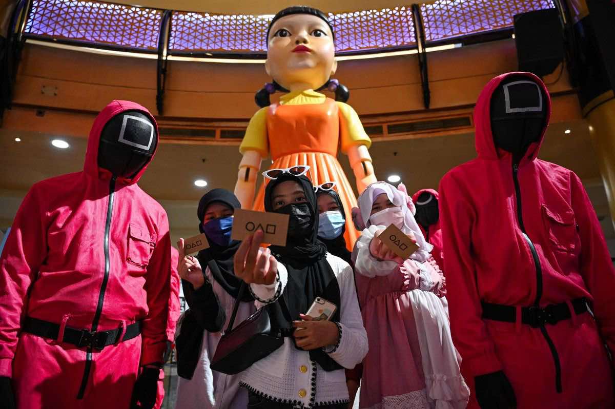 Điều gì giúp K-content chinh phục toàn cầu? Người mua sắm chụp ảnh với những người cosplay mặc trang phục trong loạt phim Squid Game của Netflix tại một trung tâm mua sắm ở Kuala Lumpur, Malaysia