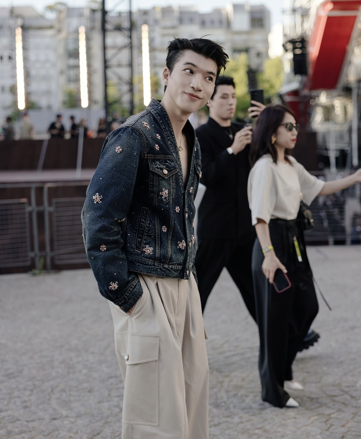 HIEUTHUHAI diện áo denim jacket màu xanh đậm với thiết kế đính hoa văn lấp lánh – một điểm nhấn tạo nên sự khác biệt và sang trọng.  Áo được mặc mở phóng khoáng, khoe khéo vòng cổ kim loại tinh tế, giúp tổng thể trở nên vừa nam tính vừa mềm mại.  Chi tiết thêu và đính hạt mang hơi hướng vintage-luxury, đúng tinh thần của Louis Vuitton.